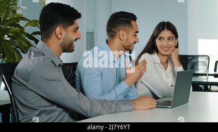 Mitarbeiter aus multiethnischen Geschäftsteams führen am Arbeitsplatz ein Brainstorming mit einem Laptop durch. Arabische, indische und mexikanische Coworkers Group diskutieren gemeinsam Corporate Stockfoto