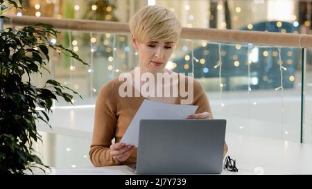 Kaukasische Geschäftsfrau mittleren Alters Lehrer Freiberufler Papierkram Sitztisch mit Laptop Papierkram Gefühl frustriert wütend wegen Fehler in Stockfoto