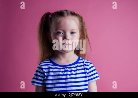 Kleines Mädchen trägt gestreiftes Kleid in einem marine Stil Reisekoffer Traum Fliegen Rest auf dem Meer Ufer rosa Hintergrund Studio Stockfoto