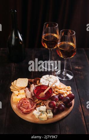 Wurst und Käse, geschnitten mit Obst, Keksen und Sauce, mit zwei Gläsern weißem Portwein und einer Flasche. Aufschnitt und Käseplatte Stockfoto