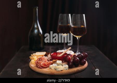 Wurst und Käse, geschnitten mit Obst, Keksen und Sauce, mit zwei Gläsern weißem Portwein und einer Flasche. Vorspeise aus Wein, Wurstwaren und Käseplatte Stockfoto