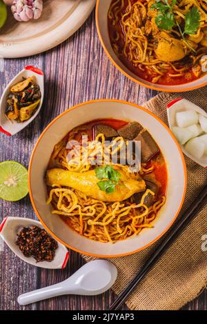 Khao Soi Kai, Blick von oben, köstliches nordthailändisches Essen, mit Gewürzen auf dem Tisch arrangiert. Stockfoto