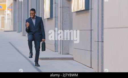 Fröhlicher, lustiger junger Geschäftsmann, der allein im Freien tanzt, feiert Freitag, Arbeitserfolg, beruflichen Erfolg, Belohnung oder Beförderung, aufgeregt Afro Stockfoto