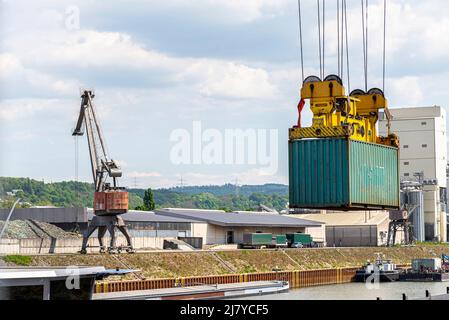 Ein Container-Portalkran auf einer Schiene lädt den Container in einen Lastkahn, der am Rheinufer in Deutschland steht. Stockfoto