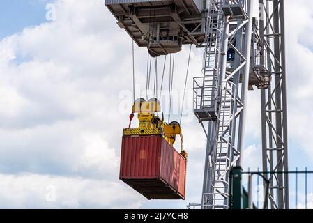 Ein Container-Portalkran auf einer Schiene lädt den Container in einen Lastkahn, der am Rheinufer in Deutschland steht. Stockfoto