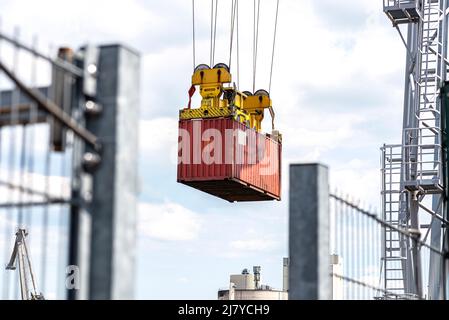 Ein Container-Portalkran auf einer Schiene lädt den Container in einen Lastkahn, der am Rheinufer in Deutschland steht. Stockfoto