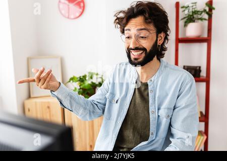 Junger Hipster-Mann, der am Laptop arbeitet und einen Videoanruf vom Heimbüro hat Stockfoto