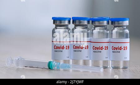 Nahaufnahme von vier Glasflaschen mit Impfmittel gegen das Covid-19-Virus Heilmittel gegen die Epidemie der Coronavirus-Immunisierung stehen auf einem Holztisch Stockfoto