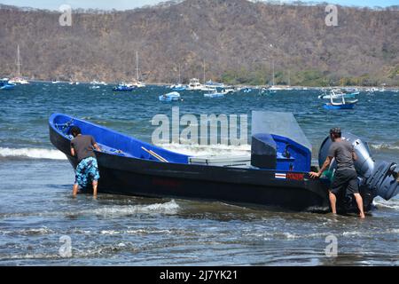 Männer schieben das Boot in die Brandung am Strand von Costa Rica Stockfoto