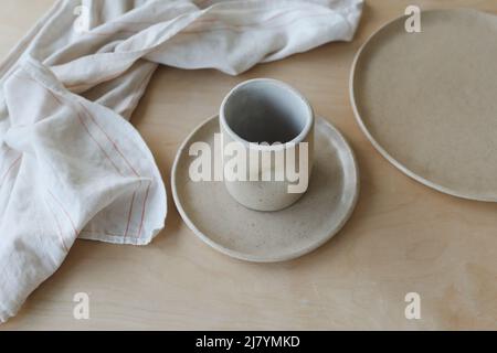Keramik Tasse und Teller auf einem Holztisch Draufsicht. Minimalistische Set von handgefertigten Keramik Geschirr und Keramik Stockfoto