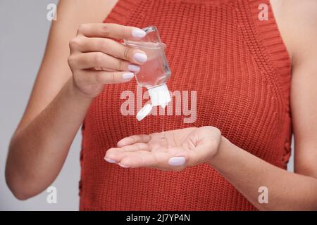 Nahaufnahme einer nicht erkennbaren Frau in orangefarbenem Strickoberteil, die antiseptisch in die Hände gießt, um sie während der Coronavirus-Epidemie zu desinfizieren Stockfoto