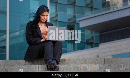 Junge Geschäftsfrau Freiberuflerin sitzt im Freien arbeiten an Internet-Typisierung auf Laptop mit Computer-Technologie tun Online-Arbeit Senden von SMS Stockfoto