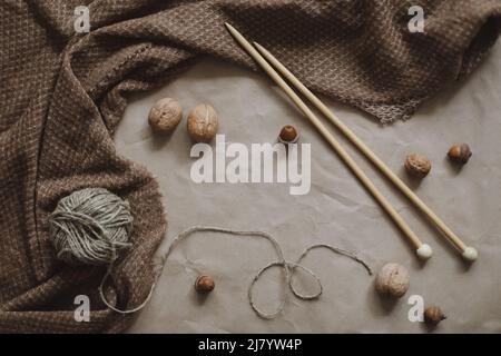 Hobby, Freizeitthema. Garn und Holznadeln auf braunem Papierhintergrund mit gemütlichem, warmem Karomuster, Draufsicht. Stockfoto
