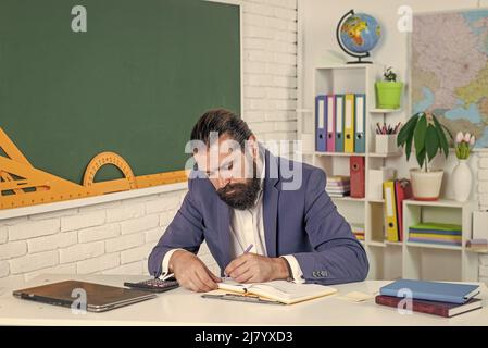 college-Dozent auf Lektion. Zurück zur Schule. Formale Bildung. Ernst reifen Lehrer Notizen in Planer. Brutal bärtigen Mann arbeiten im Klassenzimmer Stockfoto