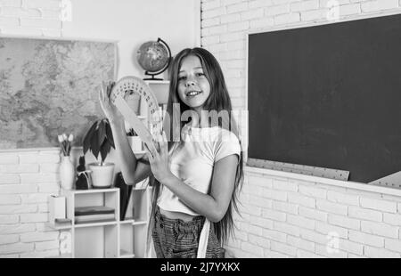 Lächelndes Teenager-Mädchen halten Winkelmesser in der Schule Klassenzimmer, Mathematik Stockfoto