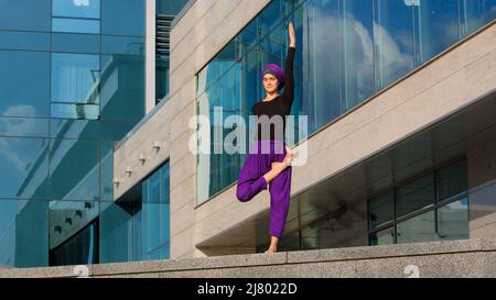 Starke muslimische Frau in Hijab Flexibles junges Mädchen dehnt Yogi Yoga Workout Baum Pose Asana weiblich hebt Bein in der Luft dabei gespaltene Strecke einen Fuß Stockfoto