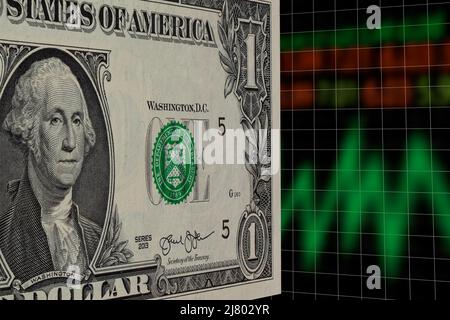 EIN US-Dollar steht in der Perspektive, mit verschwommenem Aktienindex und Chart im Hintergrund. Börsenkonzept. Stockfoto