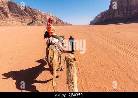 Schöne junge Frau Tourist in weißem Kleid Reiten auf Kamel in wadi Rum Wüste, Jordanien Stockfoto