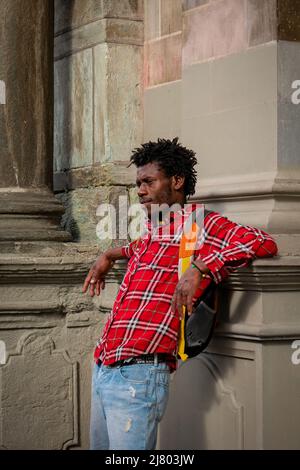 Medellin, Antioquia, Kolumbien - 8 2022. März: Schwarzer Mann mit kurzen Dreadlocks stürzt sich gegen die Mauer und beobachtet die Gruppe der Frauen beim Marsch Stockfoto