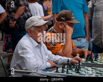 Medellin, Antioquia, Kolumbien - 8 2022. März: Kolumbianische Männer spielen auf dem Public Plaza Schach, während der feministische Marsch am Frauentag vorübergeht Stockfoto