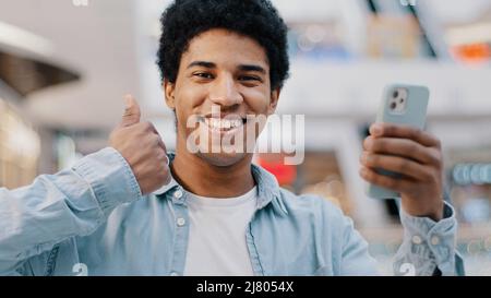 Portrait zufrieden glücklich afrikanischen Mann mit Telefon Smartphone modernes Gadget Blick auf Kamera zeigt wie Daumen nach oben empfiehlt WiFi-Handy Stockfoto