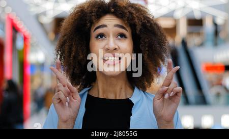 Nahaufnahme weibliches Porträt junge emotionale afroamerikanische Frau Mädchen Dame glücklich mit lockigen Haaren kreuzt Finger in der Hoffnung, um Glück zu bitten Erfolg Wunsch Stockfoto