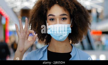 Portrait verantwortlich krank afroamerikanische Frau Mädchen Dame mit lockigen Haaren Blick auf Kamera winkende Finger kein Aufsetzen auf medizinische Schutzmaske Stockfoto