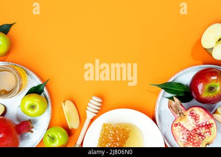Honig, Apfel und Granatapfel auf orangefarbenem Hintergrund. Konzept Jüdisches Neujahr Frohe Feiertage Rosh Hashanah. Kreatives Layout traditioneller Symbole. Anzeigen Stockfoto