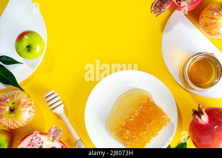 Honig, Apfel und Granatapfel auf gelbem Grund. Konzept Jüdisches Neujahr Frohe Feiertage Rosh Hashanah. Kreatives Layout traditioneller Symbole. Stockfoto