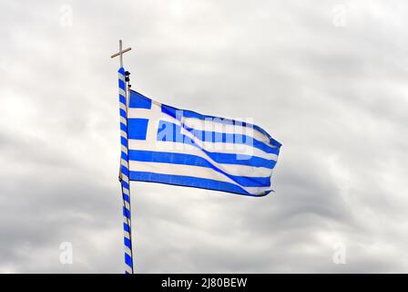 Die Nationalflagge Griechenlands sieht aus wie 9 weiße und blaue Streifen mit einem Kreuz auf dem Hintergrund eines grau bewölkten Himmels. Stockfoto