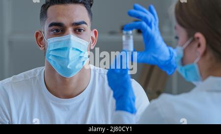 Nicht erkennbare Ärztin Krankenschwester in medizinischer Maske und Latexhandschuhen hält zeigt Flasche mit Covid-19 Impfstoff Coronavirus Heilmittel Droge auf arabisch spanisch Stockfoto