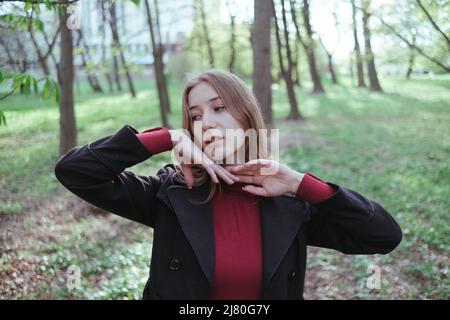 Ein Mädchen im roten Golf und einer schwarzen Jacke genießt den Frühling im Wald Stockfoto