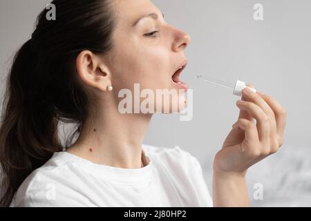 Porträt einer dunkelhaarigen jungen Frau, die Öl-Ergänzung mit Glastropfer nimmt. CBD-Hanf-Medizinöl, das auf die Zunge auftragen wird Stockfoto