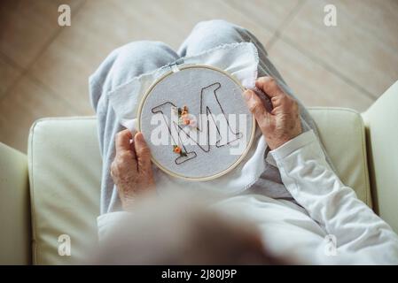 Ansicht von oben einer Frau, die einen Stickrahmen mit dem Buchstaben M hält Stockfoto