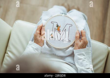 Ansicht von oben einer Frau, die einen Stickrahmen mit dem Buchstaben M hält Stockfoto