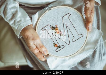 Ansicht von oben einer Frau, die einen Stickrahmen mit dem Buchstaben M hält Stockfoto