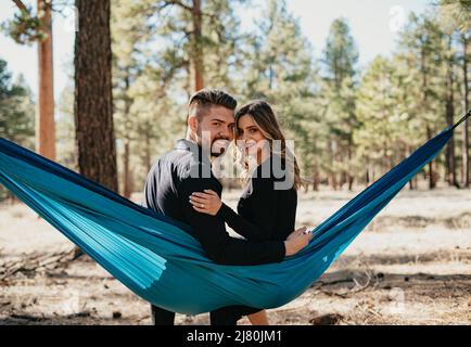 Das Paar sitzt in der Hängematte und lächelt an der Kamera Stockfoto