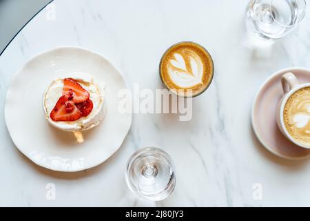 Blick von oben auf Kaffee, Wasser und Baiser-Kuchen mit frischen Erdbeeren Stockfoto