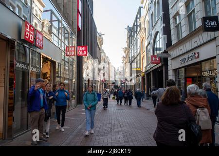 Geschäftige Einkaufsstraße in Amsterdam, an einem klaren Tag laufen Leute neben internationalen Einzelhandelsgeschäften Stockfoto