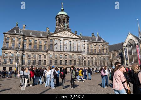 Touristen versammeln sich vor dem Königspalast auf dem Dam-Platz unter einem klaren blauen Himmel in Amsterdam, Niederlande Stockfoto