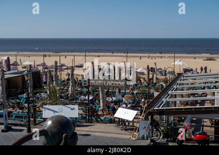 Überfülltes Strandcafé und Lounge mit Sonnenliegen und Sonnenschirmen mit Blick auf die Nordsee an einem sonnigen Tag in Scheveningen, den Haag, Niederlande Stockfoto