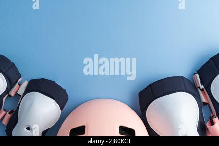 Draufsicht des Rollschuh-Schutzausrüstungssets - Knie-, Ellbogen- und Handgelenkpolster, Helm in rosa Farben. Blauer Hintergrund flach lag Stockfoto