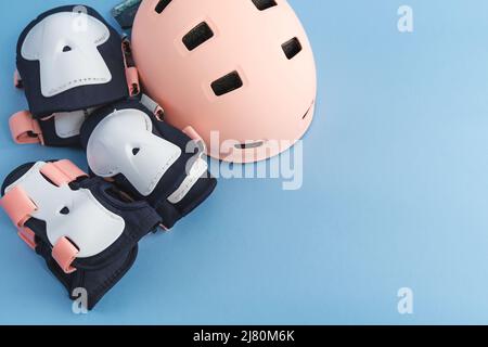 Draufsicht des Rollschuh-Schutzausrüstungssets - Knie-, Ellbogen- und Handgelenkpolster, Helm in rosa Farben. Blauer Hintergrund flach lag Stockfoto