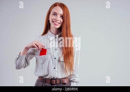 Attraktive rothaarige kaukasische Geschäftsfrau trägt gestreiftes Hemd halten Kreditkarte Studio weißen Hintergrund schwarzen freitag Verkauf Stockfoto