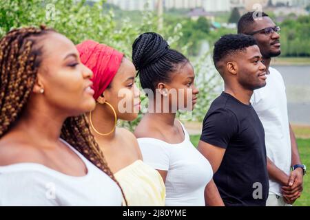 Gruppe von fünf lächelnden afroamerikanischen Männern und Frauen, die draußen bei bewölktem Wetter in der Nähe des Sees spazieren, tauschen sich mit Studenten in Russland aus Stockfoto