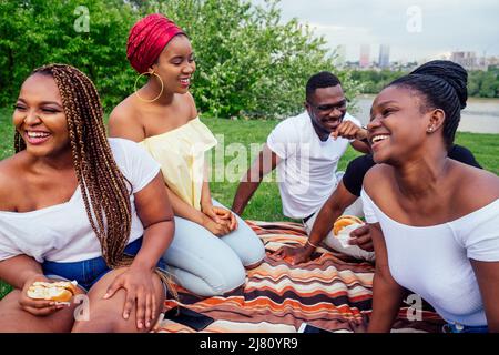 Happy Casual america african people having fun and eating Burger Outdoor Lifestyle, Studenten für eine Pause Sommerabend bewölktes Wetter im Park Stockfoto