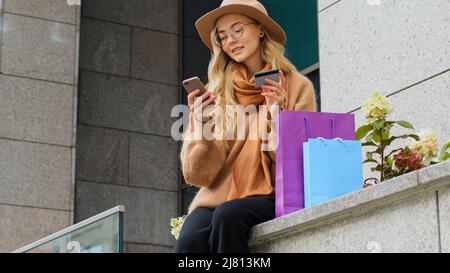 Millennial Mädchen macht Online-Shopping mit Telefon und Kreditkarte nickt Kopf affirmative weibliche custimer glücklich tanzen kaukasische Frau lächelnd Stockfoto