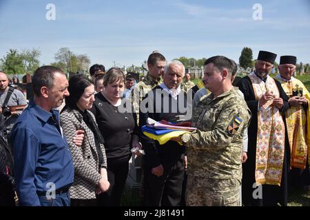 Kultschyzi, Ukraine. 11.. Mai 2022. Das Militär überreicht der Witwe des älteren Soldaten Petro Sarakulo während der Beerdigung die Flagge der Ukraine. Begräbnis des älteren Soldaten Petro Sarakulo in seinem Heimatdorf Kulchytsi, Region Lwiw. Aufgrund der russischen Militärinvasion in die Ukraine am 24. Februar 2022 ging er in die Streitkräfte der Ukraine. Er starb am 5. Mai in der Region Donezk während eines Kampfes mit den russischen Besatzern. Der Verstorbene wird von seiner Frau und zwei Kindern - Tochter Milana und Sohn Alexander - überlebt. Kredit: SOPA Images Limited/Alamy Live Nachrichten Stockfoto