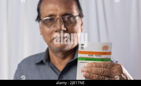 Birbhum, Westbengalen / Indien - 15. März 2022: Selektiver Fokus auf die Aadhaar-Karte, die von einem alten indischen Mann mit lächelndem Gesicht in der Hand gehalten wird Stockfoto