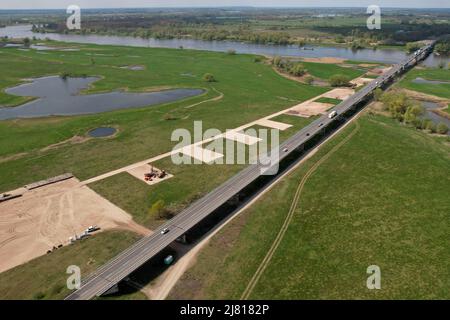 Seehausen, Deutschland. 29. April 2022. Blick auf die Brücke der Bundesstraße 189 über die Elbe Richtung Wittenberge. Daneben verläuft die Baustelle für die Elbbrücke entlang der Autobahn 14. Für den Neubau der Autobahn 14 zwischen der Anschlussstelle Seehausen-Nord (Sachsen-Anhalt) und Wittenberge (Brandenburg) beginnen in diesen Tagen die Arbeiten an der neuen Elbbrücke, die beide Länder verbindet. Zunächst beginnen südlich der Elbe die Arbeiten an den Fundamenten für die Pfeiler der Uferbrücke und des Abutments (Foto aufgenommen mit einer Drohne). Quelle: Peter Gercke/dpa/Alamy Live News Stockfoto